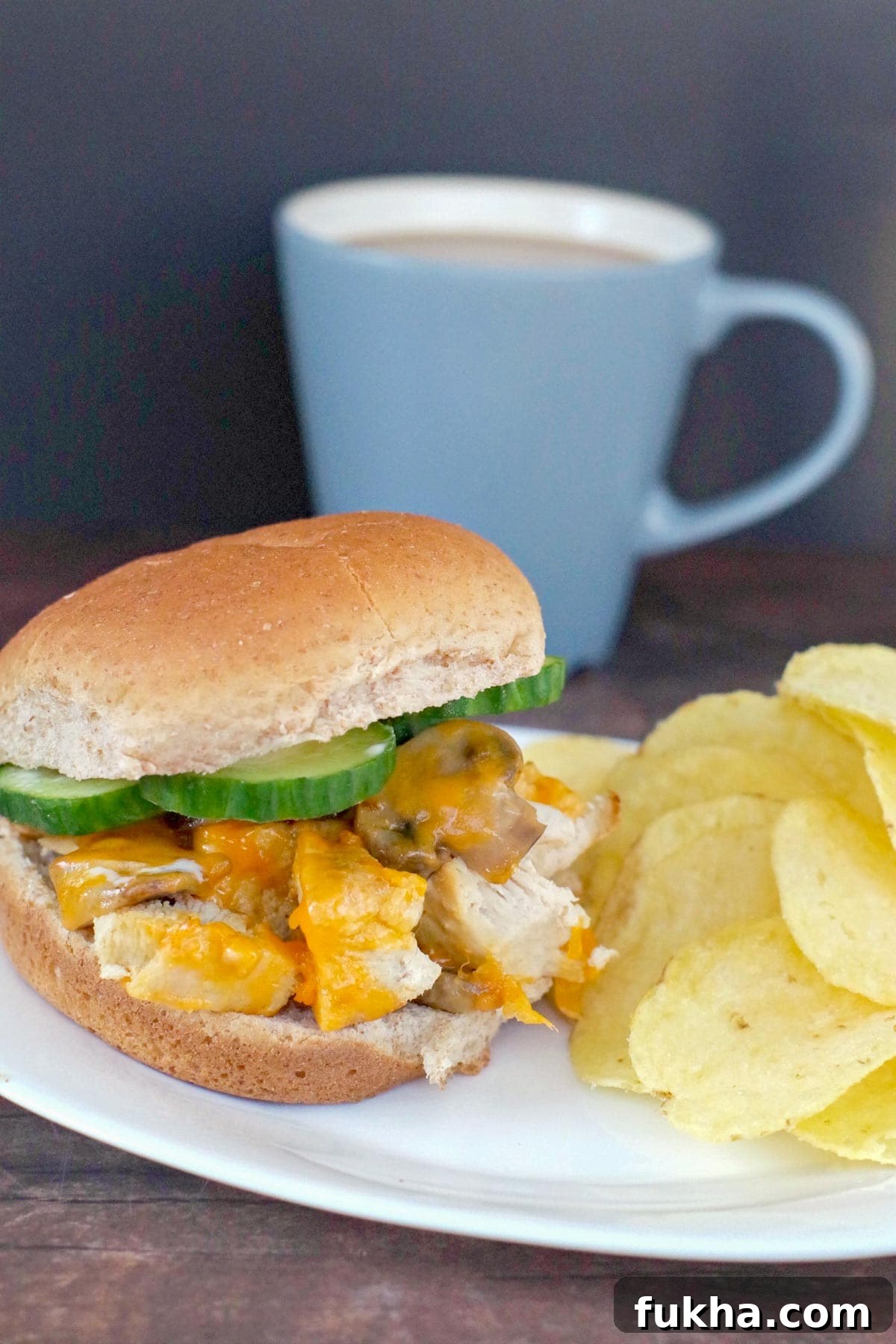 Juicy Grilled Chicken Breast Burger Recipe 9 chicken breast burger on a white plate with potato chip and blue coffee mug in the background