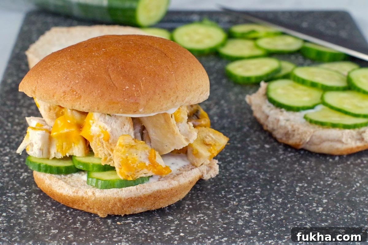 Juicy Grilled Chicken Breast Burger Recipe 10 Chicken burger on a cutting board with a ½ bun with cucumber and more cucumbers in the background