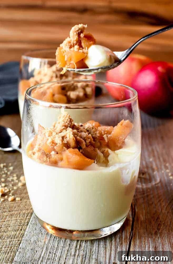 Glass of panna cotta with apple crumble topping and a spoonful being removed