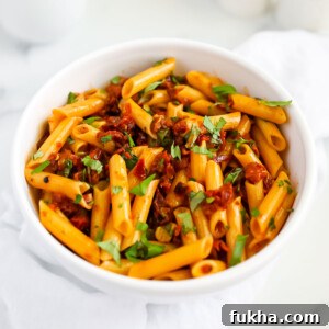 Sun Dried Tomato Pasta Recipe with Garlic and Basil 8 A white bowl filled with penne covered in a red sauce and topped with fresh green basil