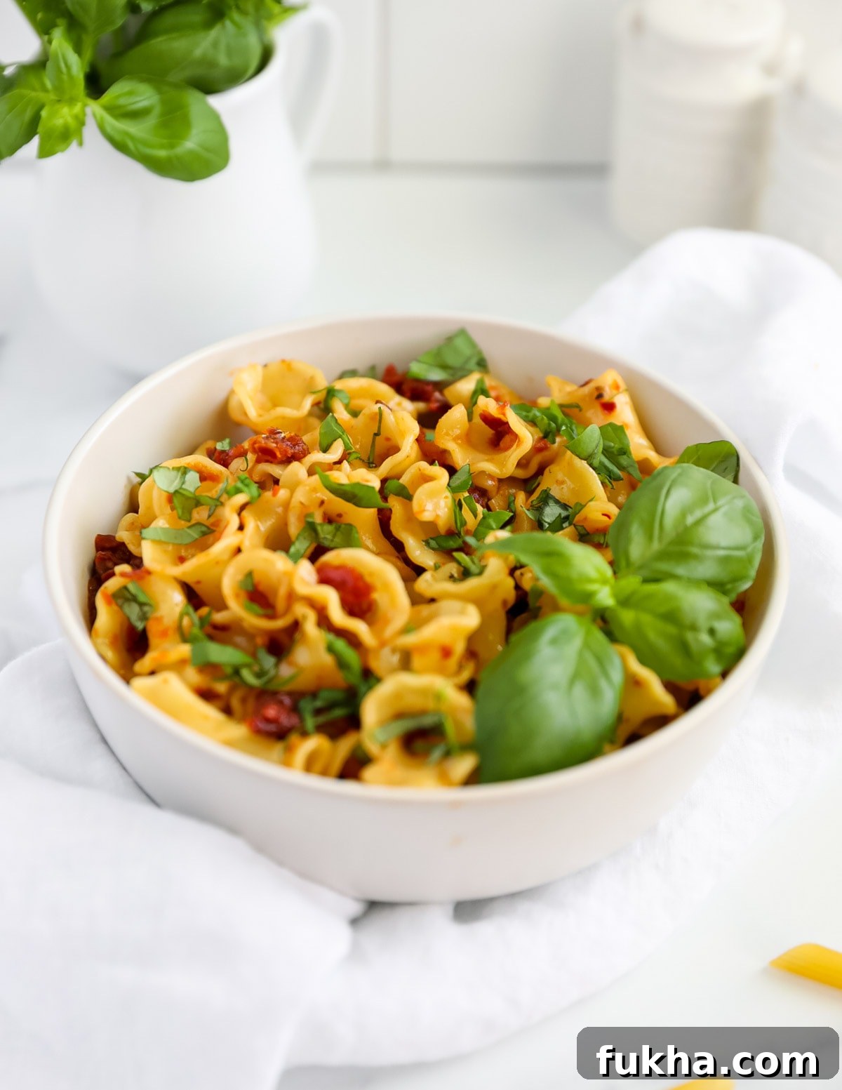 Sun Dried Tomato Pasta Recipe with Garlic and Basil 5 A bowl filled with curly pasta and red chunky pasta sauce. There is green basil on top