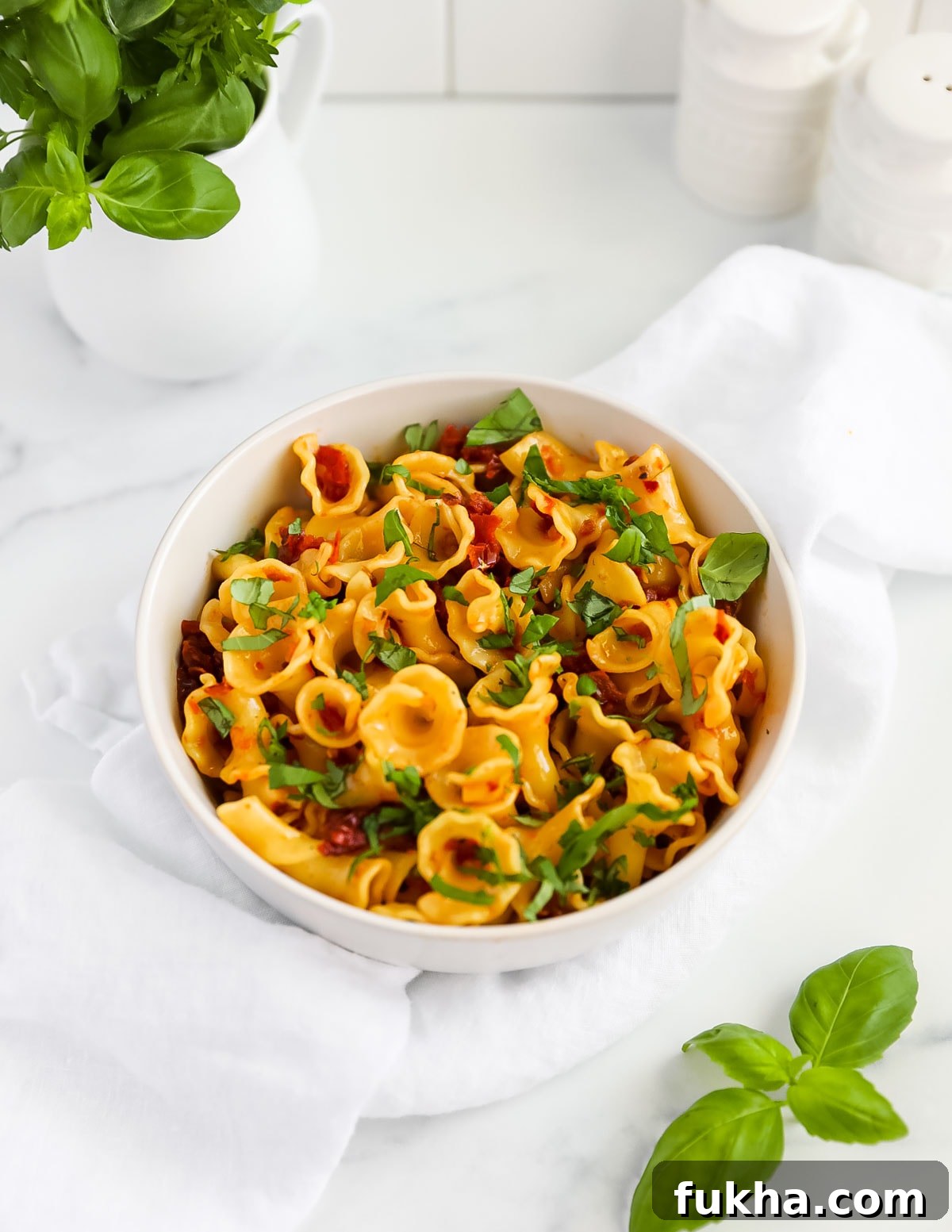 Sun Dried Tomato Pasta Recipe with Garlic and Basil 6 Curly pasta in a white bowl that is covered in fresh green chopped basil leaves