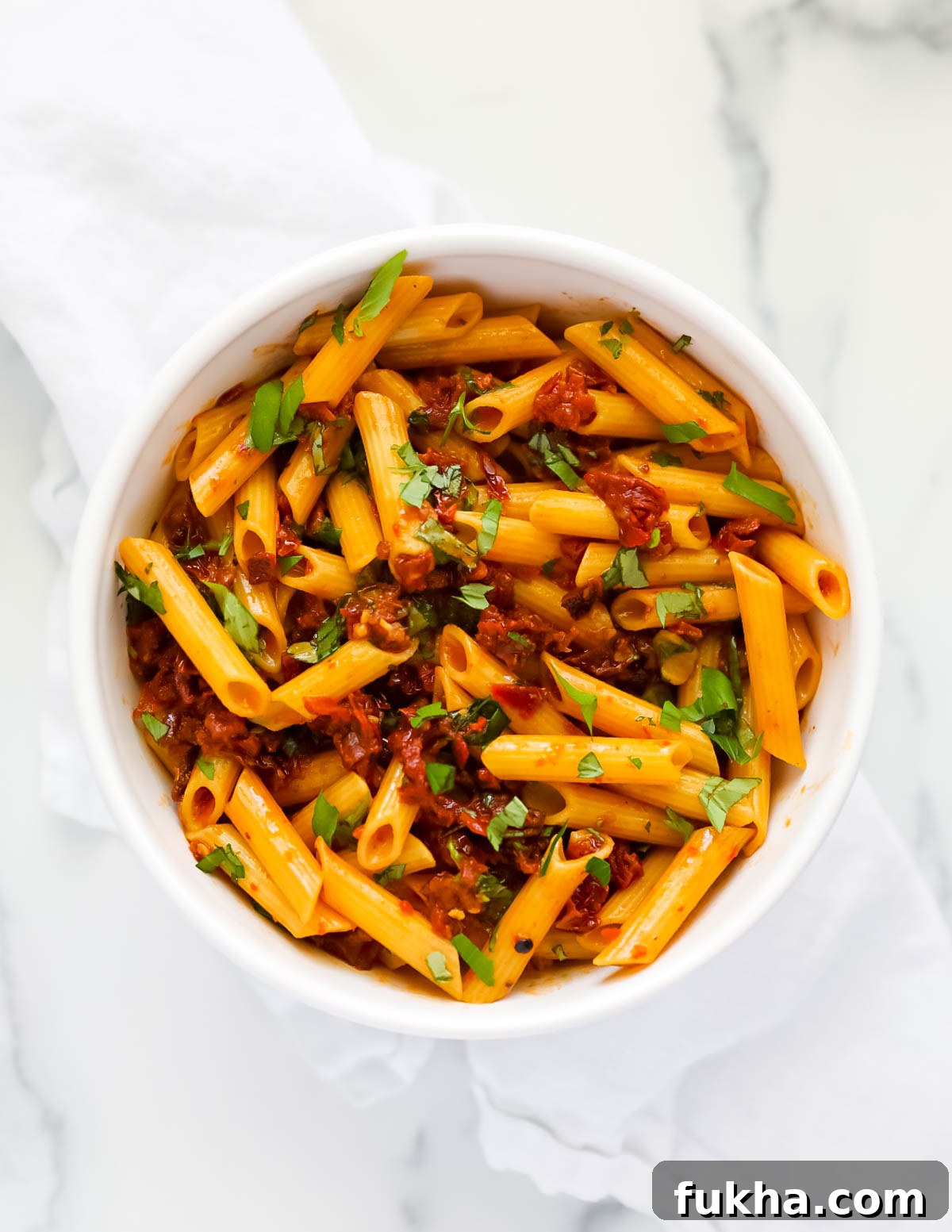 Sun Dried Tomato Pasta Recipe with Garlic and Basil 7 An overhead picture of pasta that is covered in a chunky red sauce and fresh basil leaves