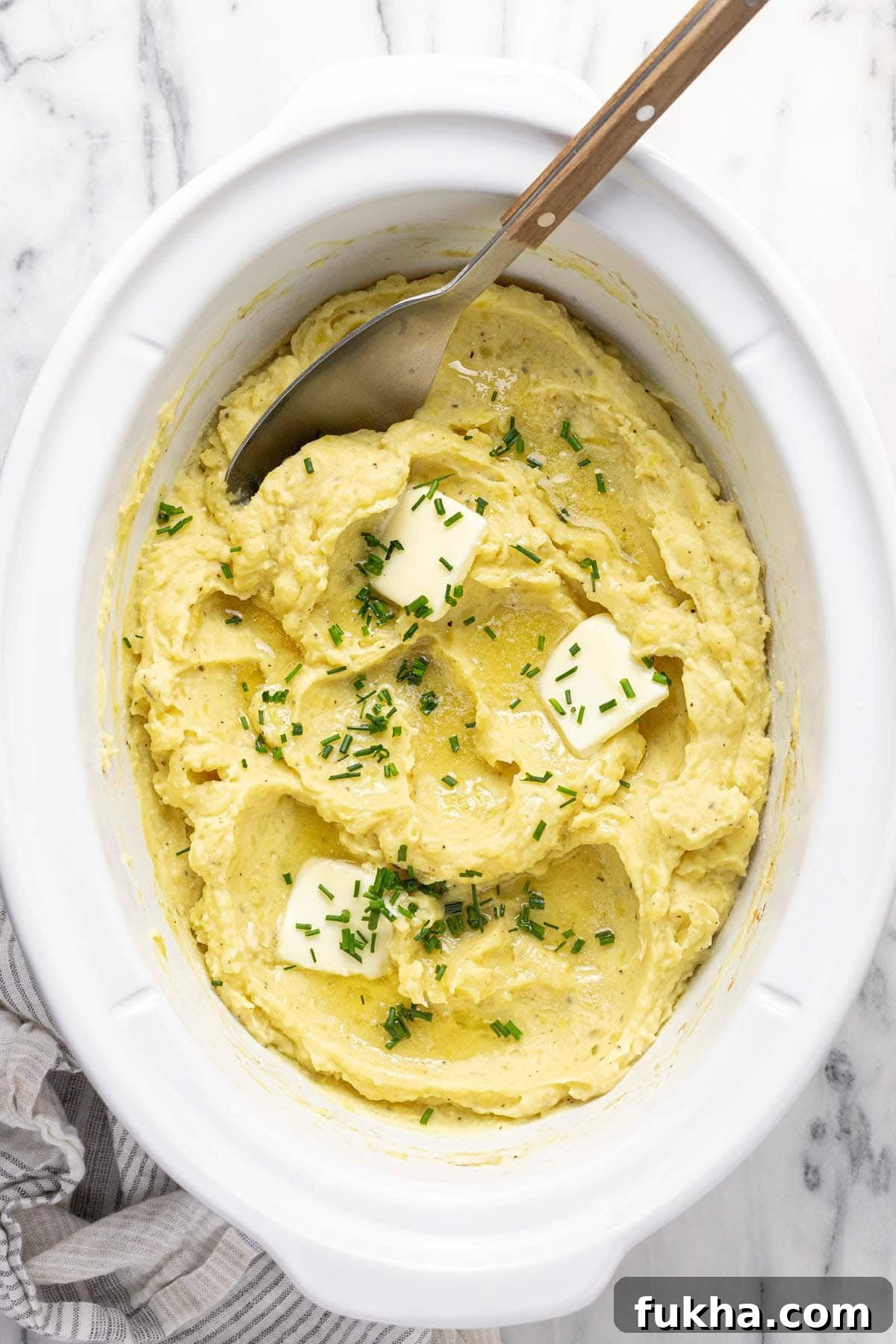 Creamy Slow Cooker Mashed Potatoes 7 Crock pot insert filled with creamy homemade mashed potatoes garnished with butter and chives.