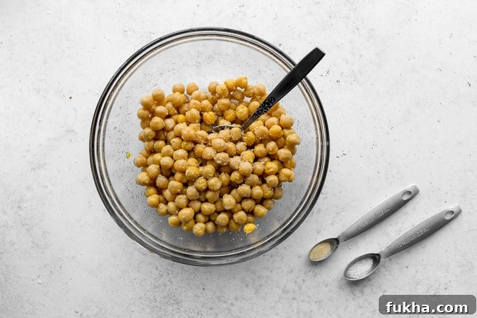 Chickpeas in a glass bowl with seasoning being stirred in.