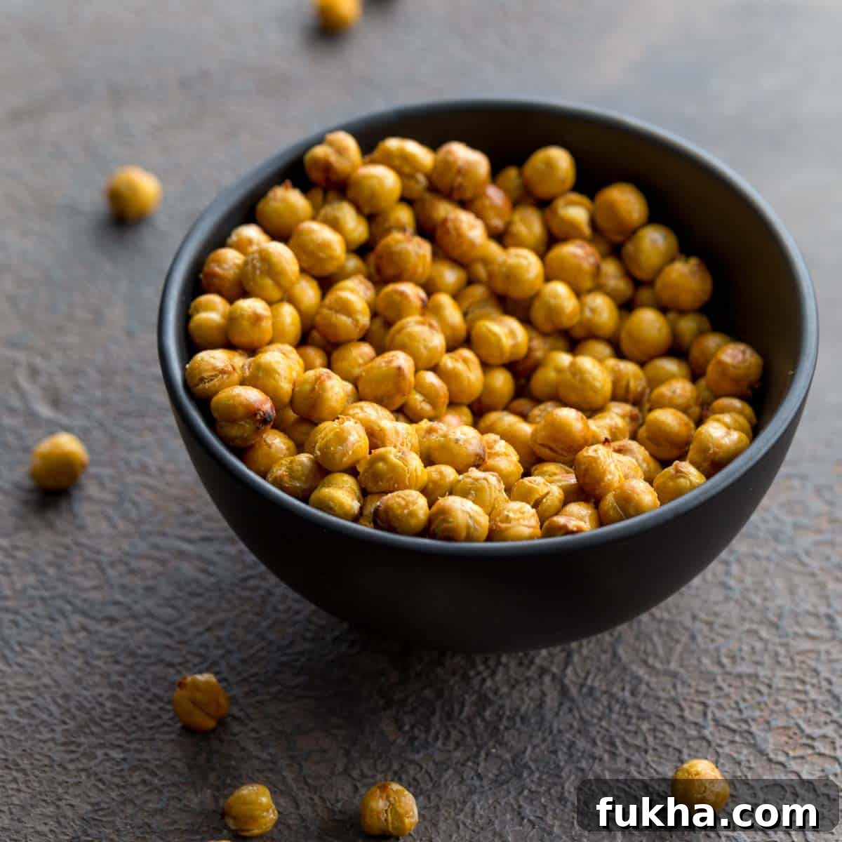 Air fryer chickpeas in a small black bowl with some chickpeas scattered around the bowl.