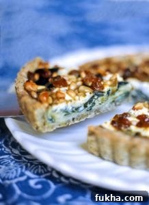 A swiss chard, leek, and goat cheese tart on a white platter with one slice being cut.