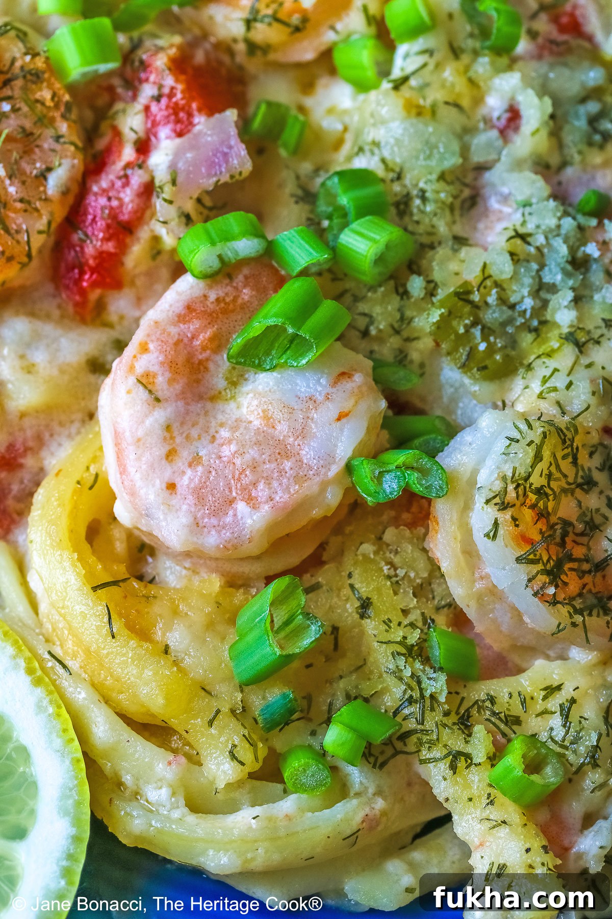 Large scoop of Creamy Dill Shrimp Casserole with shrimp on top and also with peas, yellow squash, and lemon slices on a dark blue plate sitting on a pale blue and white striped cloth © 2025 Jane Bonacci, The Heritage Cook.