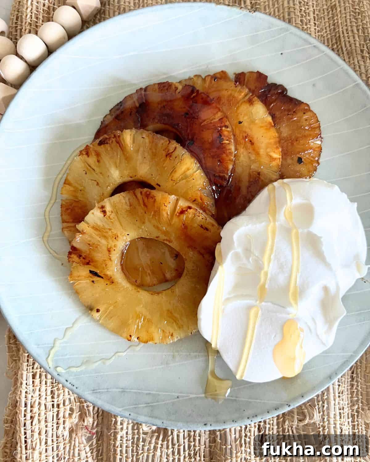 Sliced grilled pineapple next to cool whip on a blue plate drizzled in honey.
