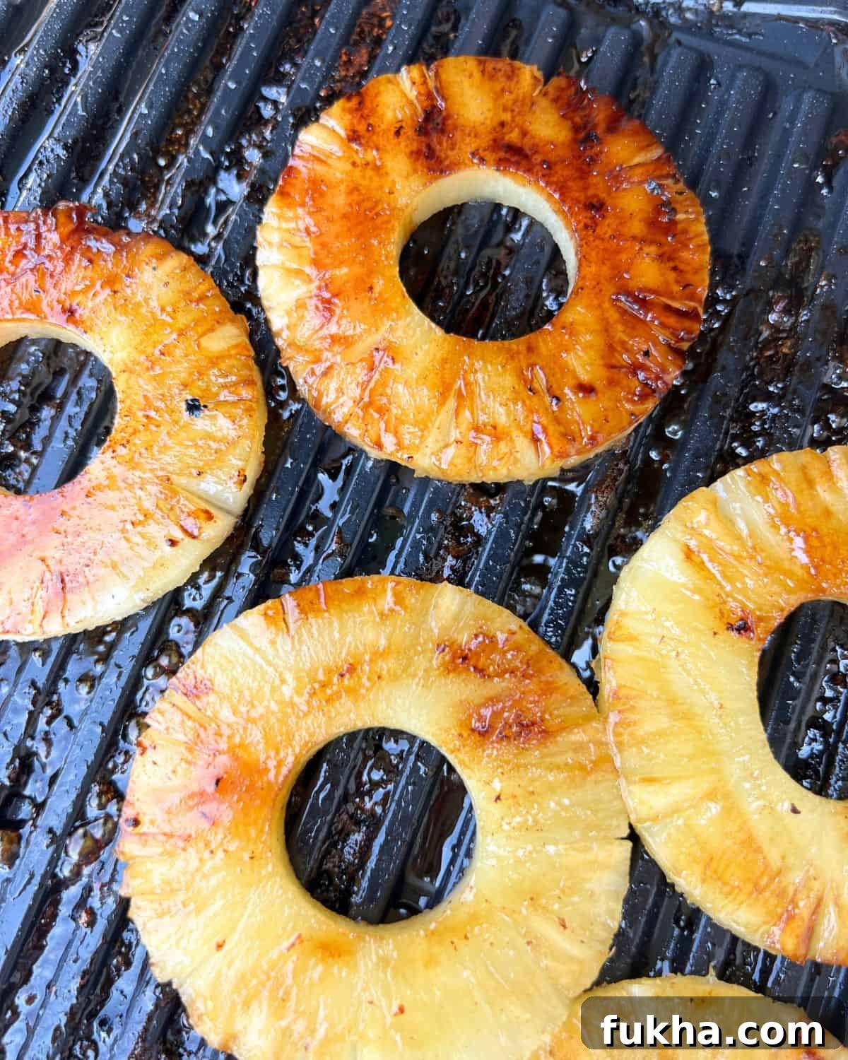 Marinated pineapple cooking on a grill.