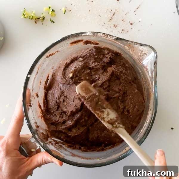 Fudgy Gluten Free Double Chocolate Zucchini Banana Muffins 10 Mixing the muffin batter and a glass mixing bowl with a spatula.