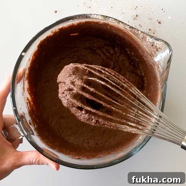 Fudgy Gluten Free Double Chocolate Zucchini Banana Muffins 9 Mixing the muffin batter with a whisk in a glass mixing bowl.
