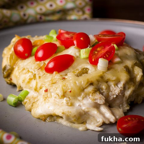 A plate of Chicken Enchiladas Verdes topped with fresh tomatoes and green onions.