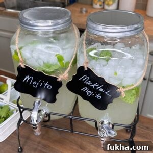 Two large glass beverage dispensers filled with ice, lime slices, and mint leaves sit on a counter. One is labeled Mojito and the other Mocktail Mojito. Both have spouts for pouring.