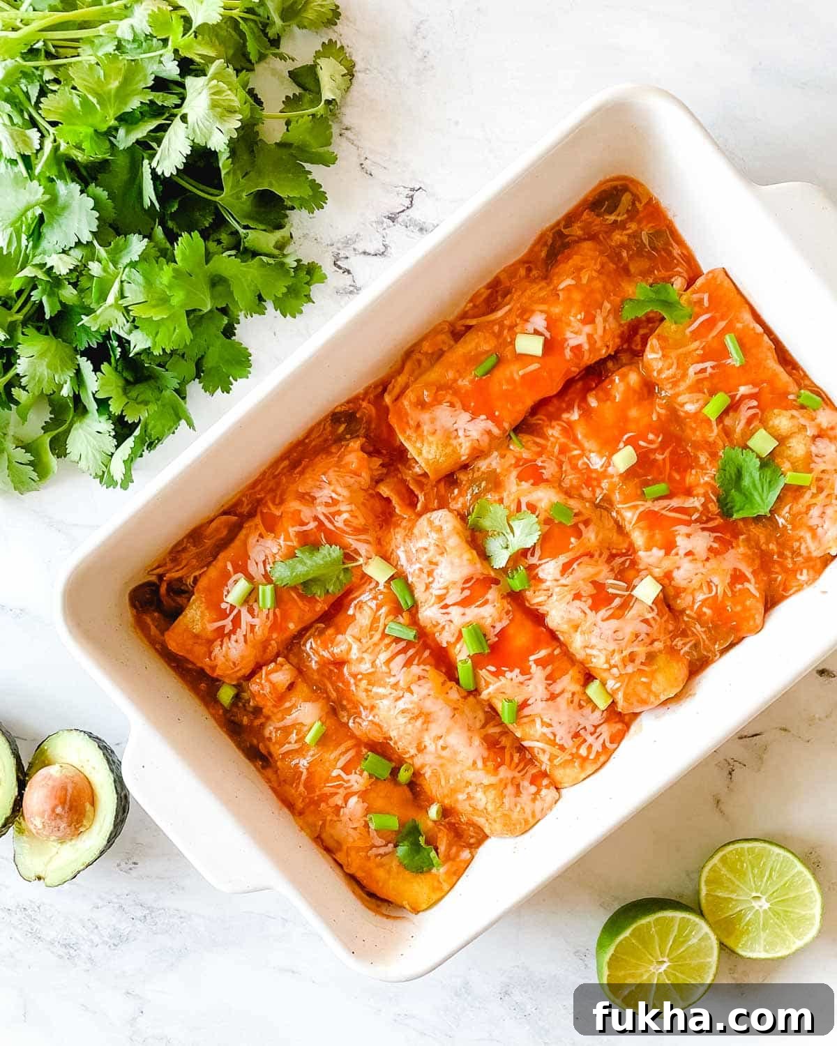 Slow Cooker Shredded Chicken Enchiladas 2 A baking dish full of chicken enchiladas is surrounded by cut limes, a halved avocado, and cilantro.