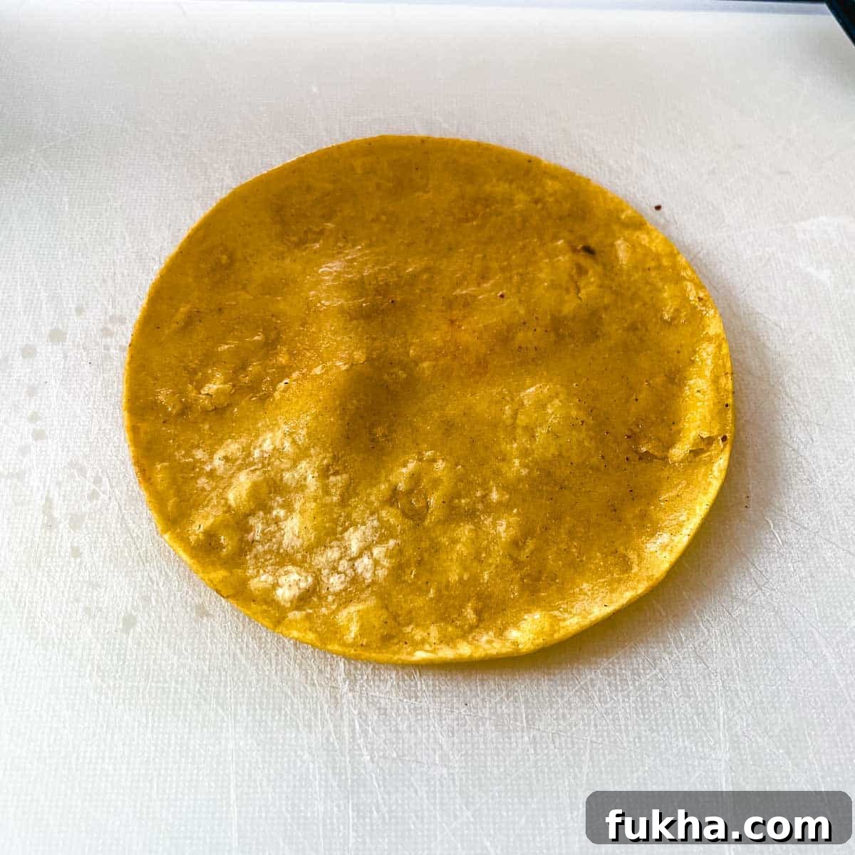 Slow Cooker Shredded Chicken Enchiladas 10 A fried corn tortilla sits on a white cutting board.