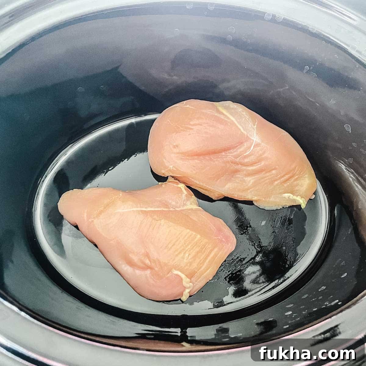 Slow Cooker Shredded Chicken Enchiladas 5 Two chicken breasts are placed in the base of a slow cooker.