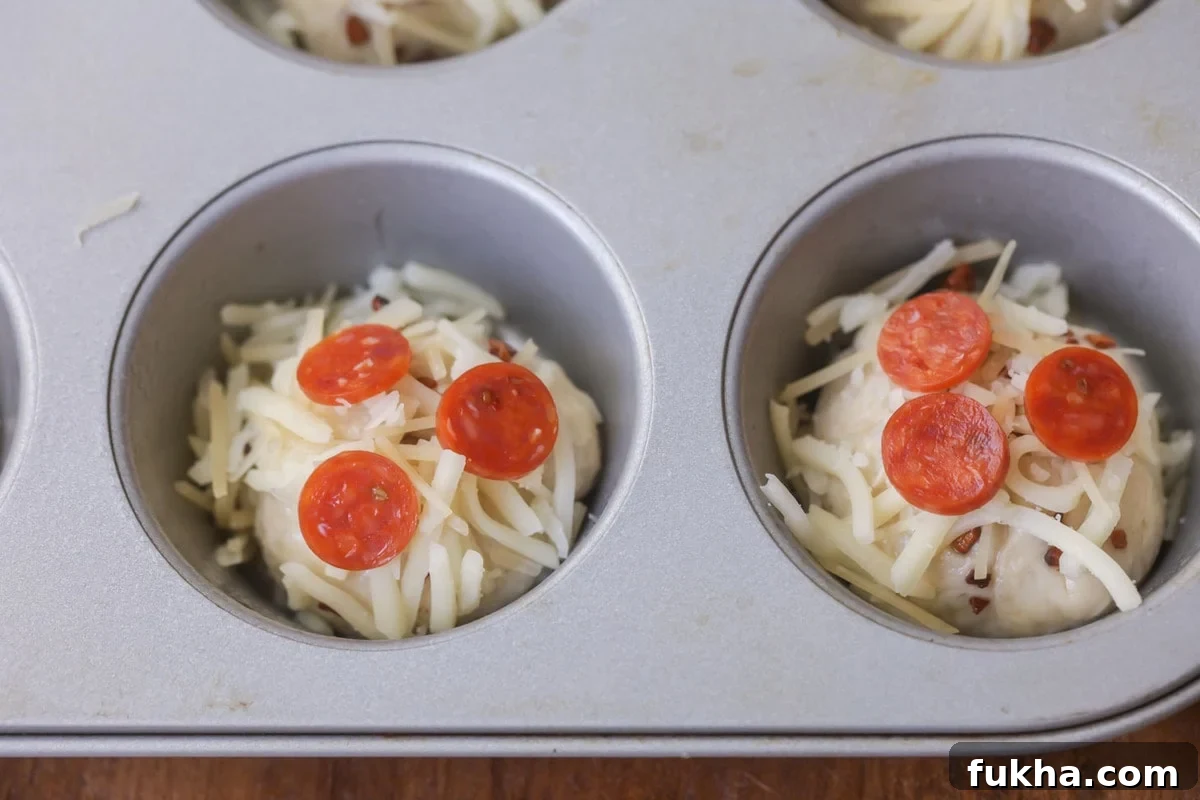 Muffin tin pizzas topped with mini pepperonis ready to be baked.