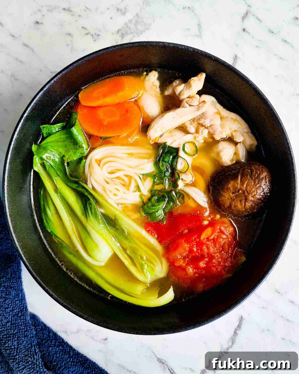 A bowl of noodle soup topped with chicken and vegetables