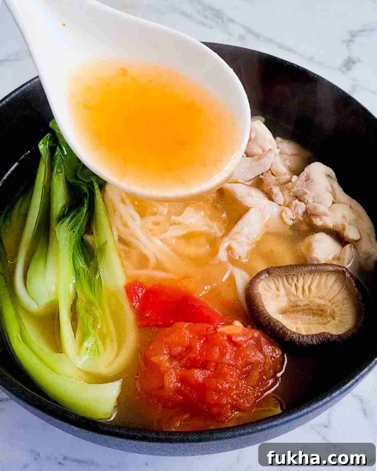 Soup being poured into a bowl of noodle soup