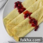 Close up of 3 Swedish pancakes on a plate topped with lingonberries.