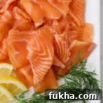 Close up of gravlax on a white platter with dill and lemons.