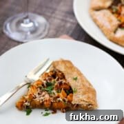 Slice of Butternut Squash Galette on a white plate next to a fork and glass of wine.