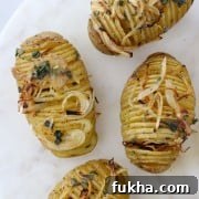 Hasselback potatoes topped with herbs and onions on a marble surface