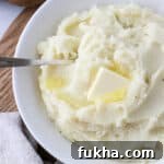 Overhead shot of mashed potatoes in a white bowl topped with butter with a spoon.