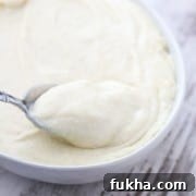 A bowl of potato and celery root puree with a spoon on a wooden surface