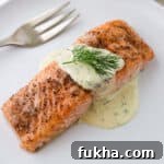 Close up of baked salmon topped with Warm Mustard Dill Sauce and a sprig of dill.
