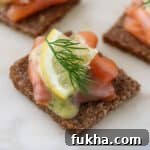Close up of gravlax on rye bread topped with a lemon wedge and fresh dill.