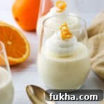 Light and Creamy Orange Mousse in a a glass next to a spoon and an orange.