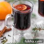 A cup of mulled wine next to evergreen branches, spices and an orange.