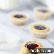 Raspberry thumbprint cookies on a marble surface with a glass of milk.