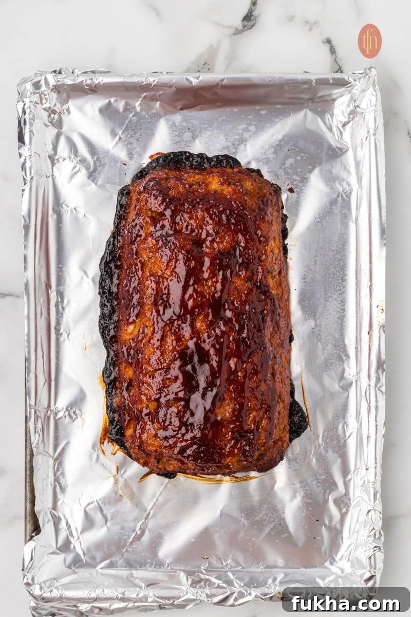 An overhead shot of the fully baked chicken meatloaf on the foil-lined baking sheet, covered in a glossy, dark red glaze.