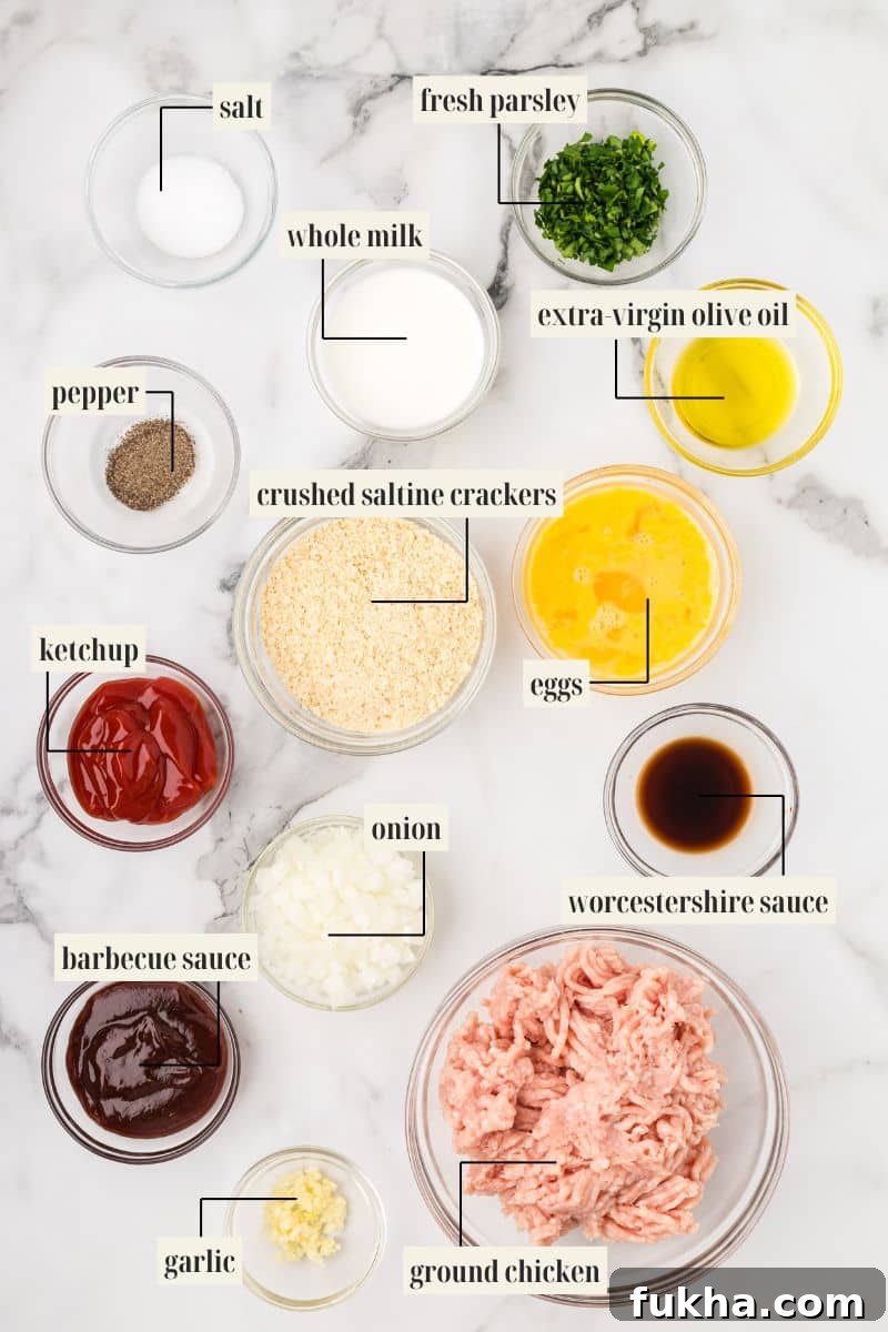 A flat lay of the labeled ingredients for ground chicken meatloaf: salt, pepper, ketchup, barbecue sauce, garlic, whole milk, crushed saltine crackers, diced onion, ground chicken, fresh parsley, extra virgin olive oil, eggs, and Worcestershire sauce.