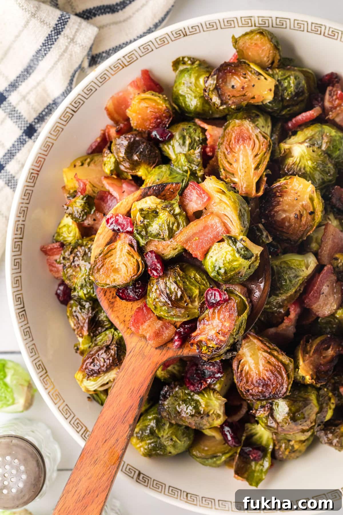 Roasted brussels sprouts with bacon and cranberries being spooned out of the serving bowl with a wooden spoon.