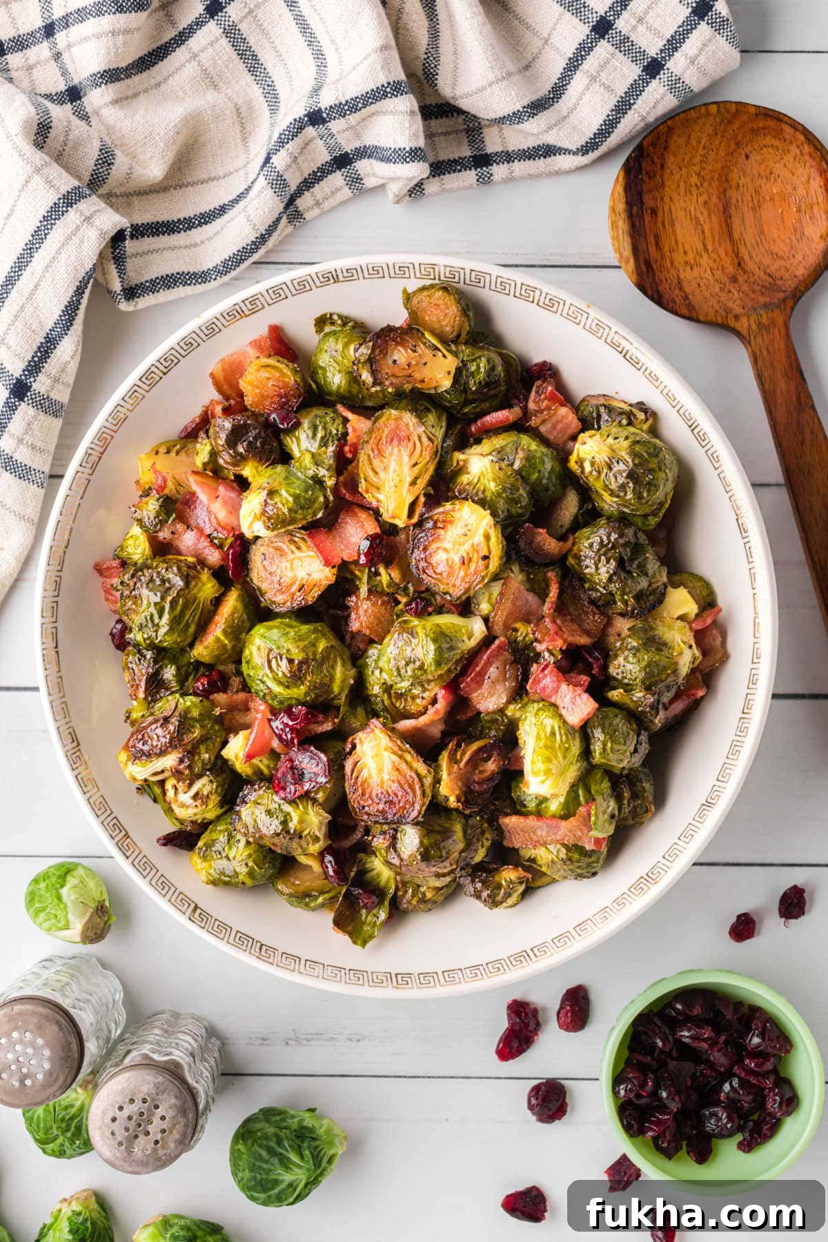 Crispy bacon and Brussels sprouts are shown in a white bowl with cranberries tossed in.
