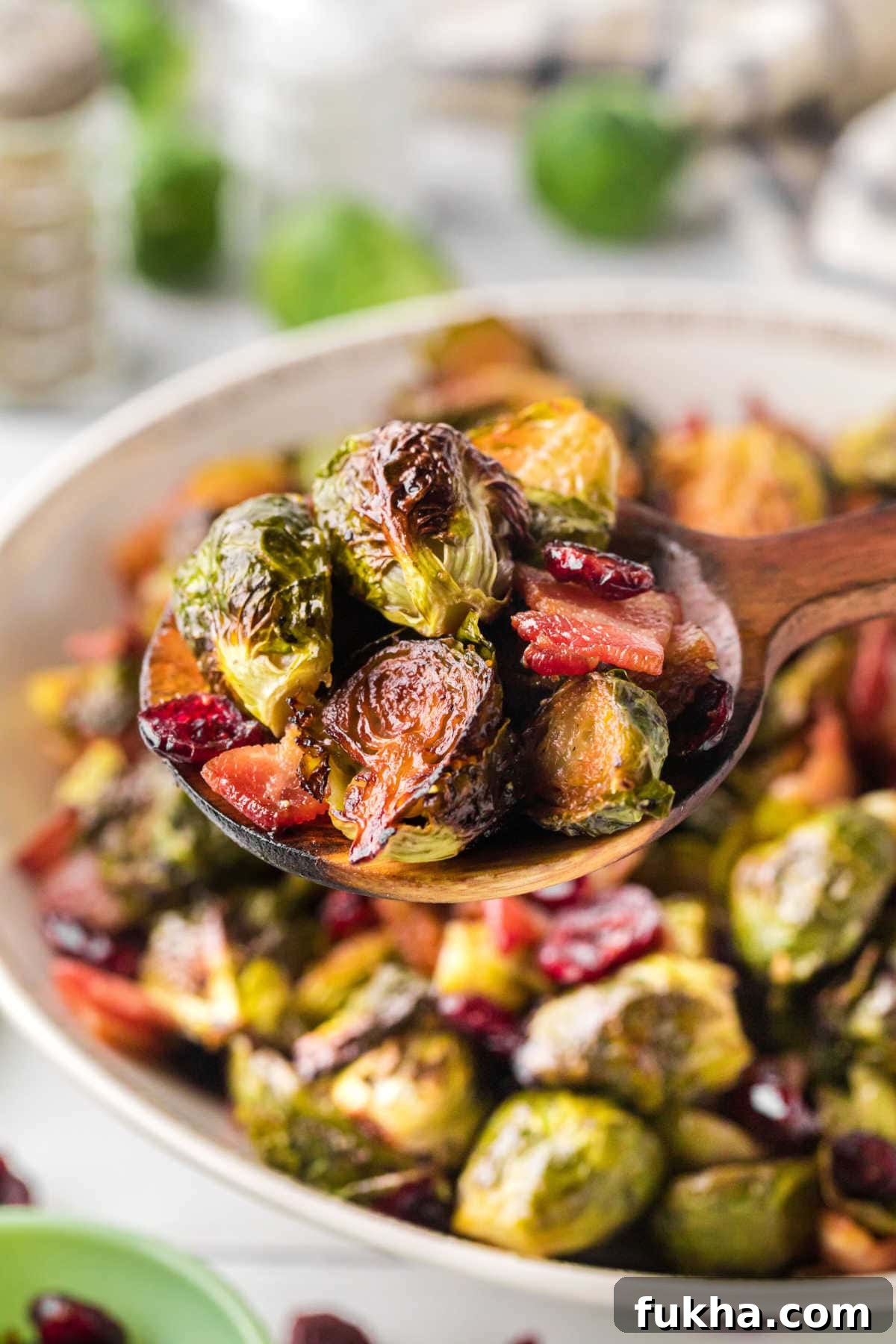 Wooden spoon scooping roasted Brussels sprouts with bacon and cranberries from a bowl.