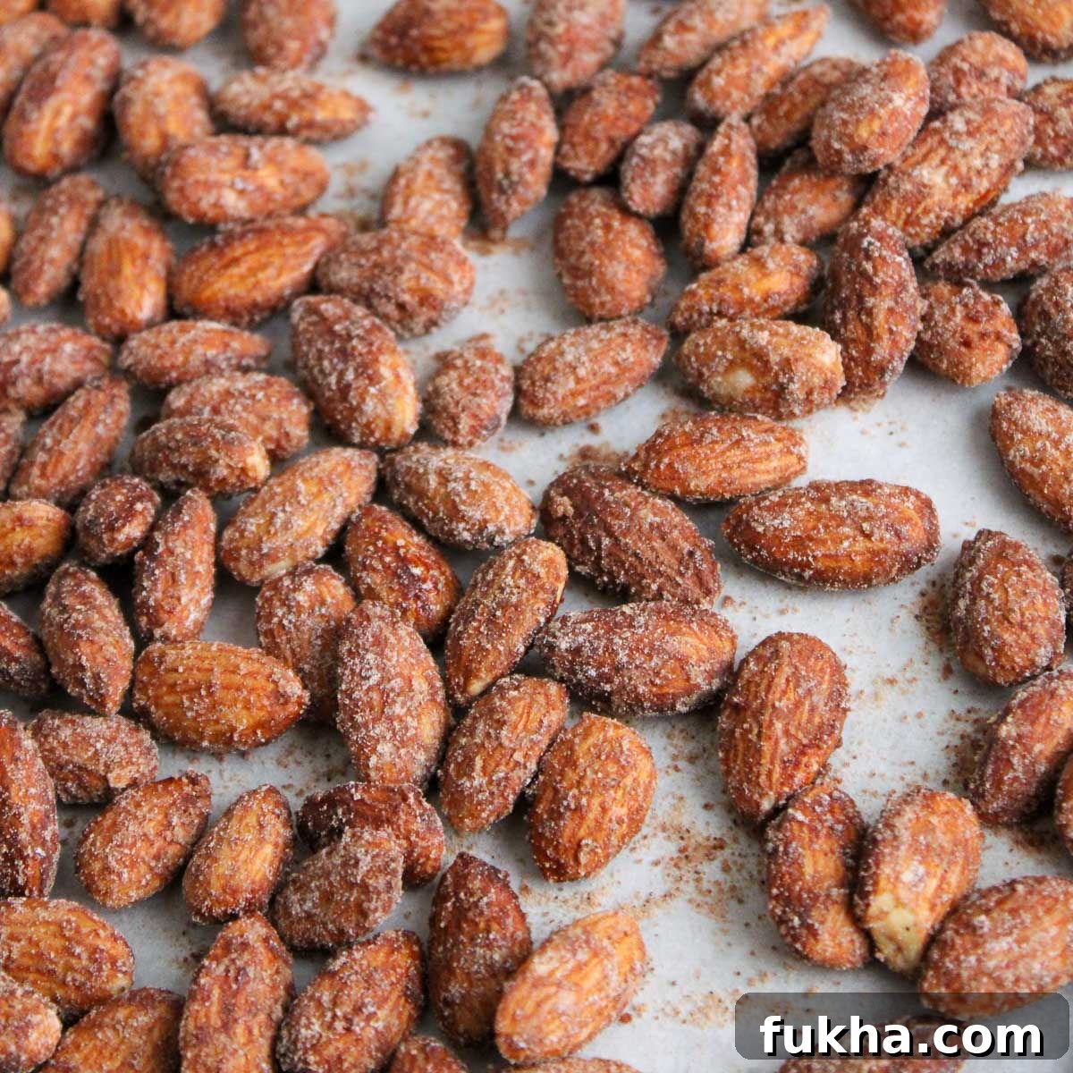 The cinnamon almonds on a parchment paper lined sheet pan cooling down.