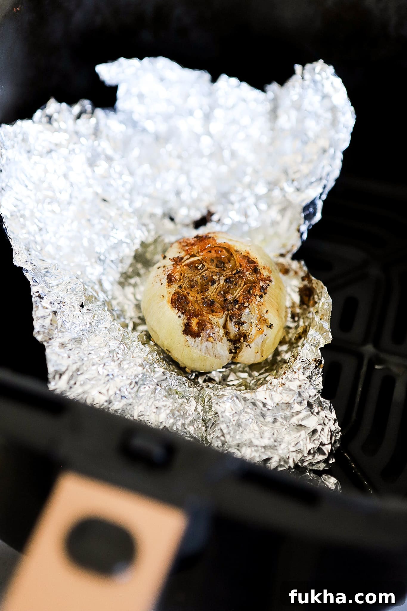 view of the top of the garlic bulb in aluminum foil in the air fryer